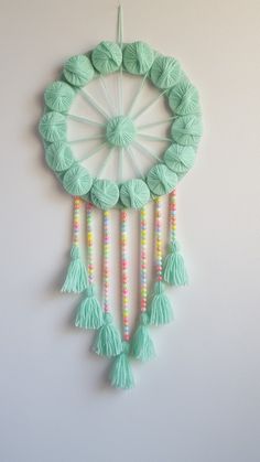 a green wall hanging with tassels and beads in the shape of a wheel