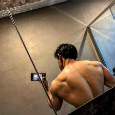 a shirtless man taking a selfie in front of a mirror with his cell phone