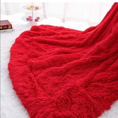 a large red blanket on top of a white bed next to a book and cup