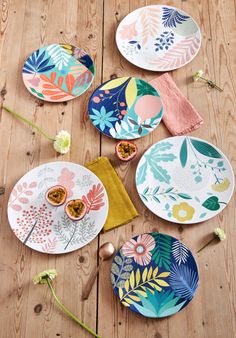 four plates with different designs on them sitting on a wooden table next to flowers and napkins