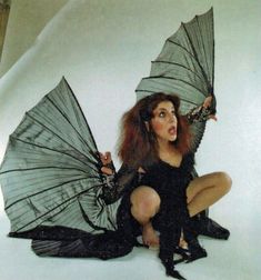 a woman is dressed in black and holding two umbrellas while sitting on the ground