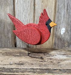 a red bird sitting on top of a wooden table next to a wood plank wall