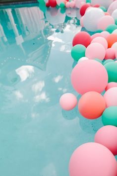 there are many balls floating in the water near each other and one is pink, green, and blue