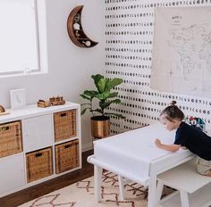 a little boy sitting at a white table in front of a drawing on the wall