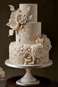 a three tiered wedding cake with white flowers on the top and bottom, sitting on a pedestal