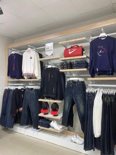 clothes and shoes are displayed on shelves in a clothing store, including sweatshirts and jeans