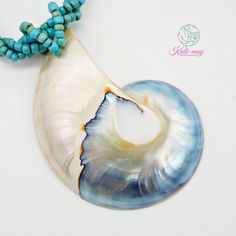 a blue and white shell with turquoise beads on it's end, next to a beaded necklace