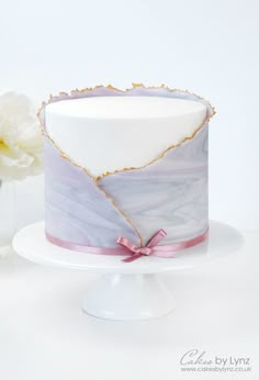 a white and purple marble cake with pink ribbon on a plate next to a flower