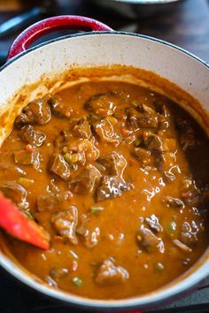 a pot full of stew sitting on top of a stove next to a red spatula