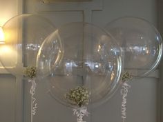 three clear balloons are hanging from the ceiling in front of a wall with flowers and ribbons