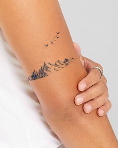 a woman's arm with a tattoo on it that has mountains and birds flying in the sky