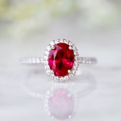 a close up view of a ring with a red stone in the center and white diamonds around it