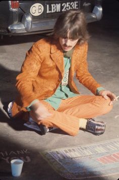 a young man sitting on the ground in front of a car