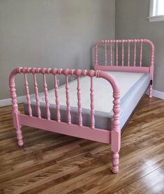 a pink bed frame sitting on top of a hard wood floor next to a window