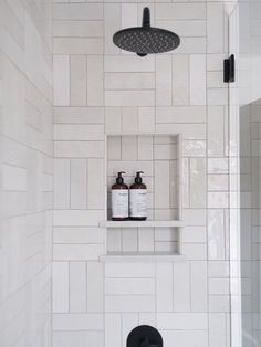 a white tiled bathroom with black fixtures and shelves on the wall, along with two soap dispensers