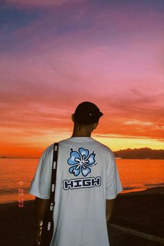 a man standing on top of a beach next to the ocean under a colorful sky