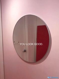 a round mirror hanging on the side of a wall next to a door with an inscription that reads, you look good