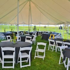 tables and chairs are set up under a tent for an outdoor function in the grass