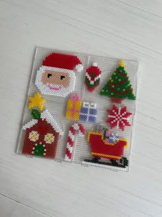 a cross stitch christmas scene with santa claus and other decorations on a white table top