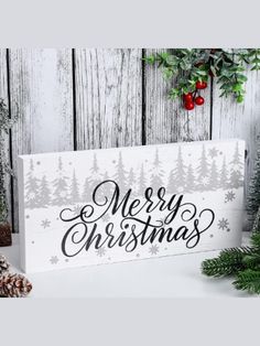 a wooden sign that says merry christmas with pine trees and evergreens in the background