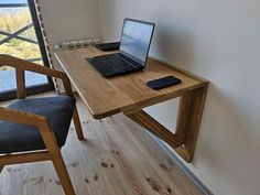 a laptop computer sitting on top of a wooden desk next to a chair and window