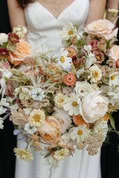 a bride holding a bouquet of white and peach flowers in her hands while standing next to the groom