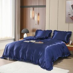 a bed with blue comforter and pillows in a room next to a lamp on a table