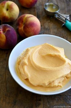 a white bowl filled with peanut butter next to some peaches on a wooden table