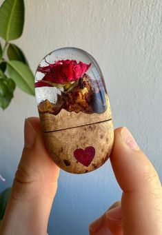 a hand holding a rock with flowers in it and a heart on the inside, sitting next to a potted plant