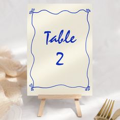 a table number sign sitting on top of a wooden easel next to a fork