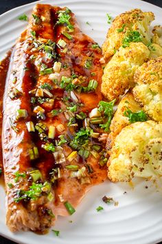 a white plate topped with meat, cauliflower and broccoli covered in sauce