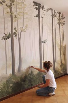 a woman is painting a mural on the wall in front of a wood paneled forest