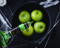 green apples in a black bowl with an empty bottle