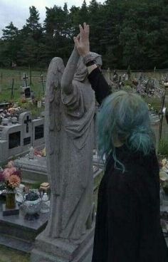 a woman with green hair standing in front of a grave yard holding her hands up to the sky