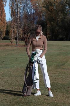 a woman standing in the grass with her hand on her hip and wearing white pants