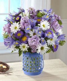 a blue vase filled with purple and white flowers next to a bird's nest