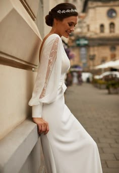 a woman in a white dress leaning against a wall