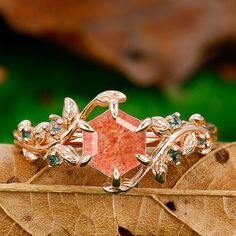 a ring with an orange stone surrounded by green and white stones on top of a leaf