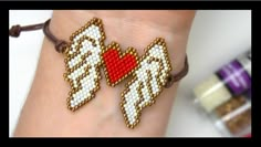 a bracelet with two white angel wings and a red heart in the middle on someone's wrist