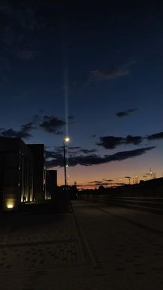 an empty street at night with the sun setting in the distance and clouds lit up