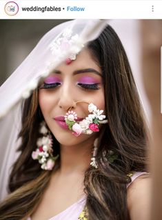 a woman with flowers on her nose and veil over her head, wearing purple makeup