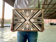 a person holding up a wooden box with an abstract design on it's side