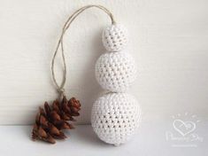 two white crocheted balls sitting on top of each other next to a pine cone