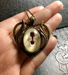 a hand holding a pendant with a spider on it's face and an egg in the middle