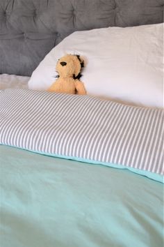 a teddy bear sitting on top of a bed with white sheets and blue pillow cases