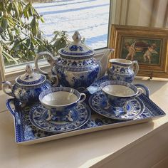 a blue and white tea set sitting on top of a tray next to a window