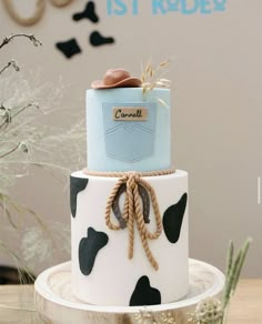 a three tiered cake decorated with black and white cow print, blue ribbon, and brown booties