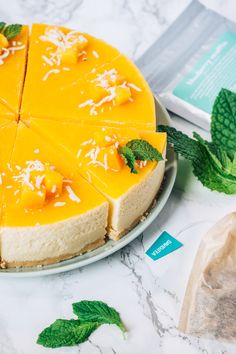 a cheesecake on a plate next to mint leaves and a packet of tea in the background