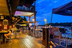 people sitting at tables on a deck overlooking the water