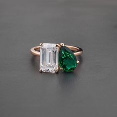 an emerald and diamond ring sitting on top of a black surface with one stone in the middle